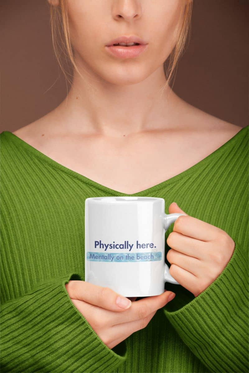 sarcastic beach lover mug with a person holding a mug with text 'Physically here, mentally on the beach' against a brown background
