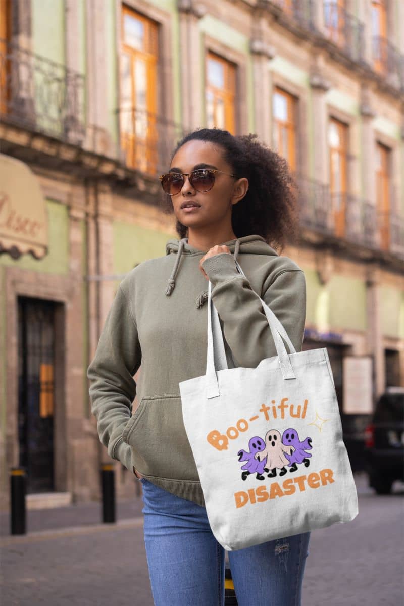 scary cute tote with a woman holding a tote bag with 'Boo-tiful Disaster' design on a city street.