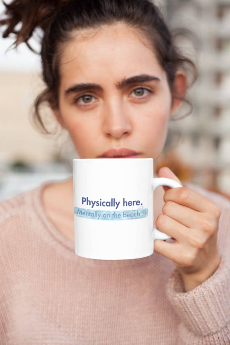 vacation morning coffee mug with a person holding a mug with text 'Physically here. Potentially on the beach.'