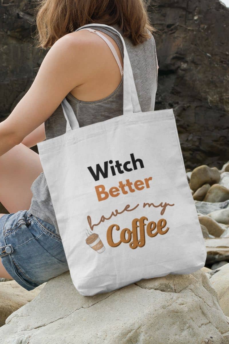 witch humor tote with a person holding a tote bag with text 'Witch Better Have My Coffee' on a rocky beach