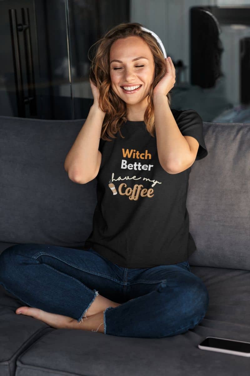 witch humor t-shirt with a woman wearing a black t-shirt with text 'Witch Better Have My Coffee', sitting on a couch.