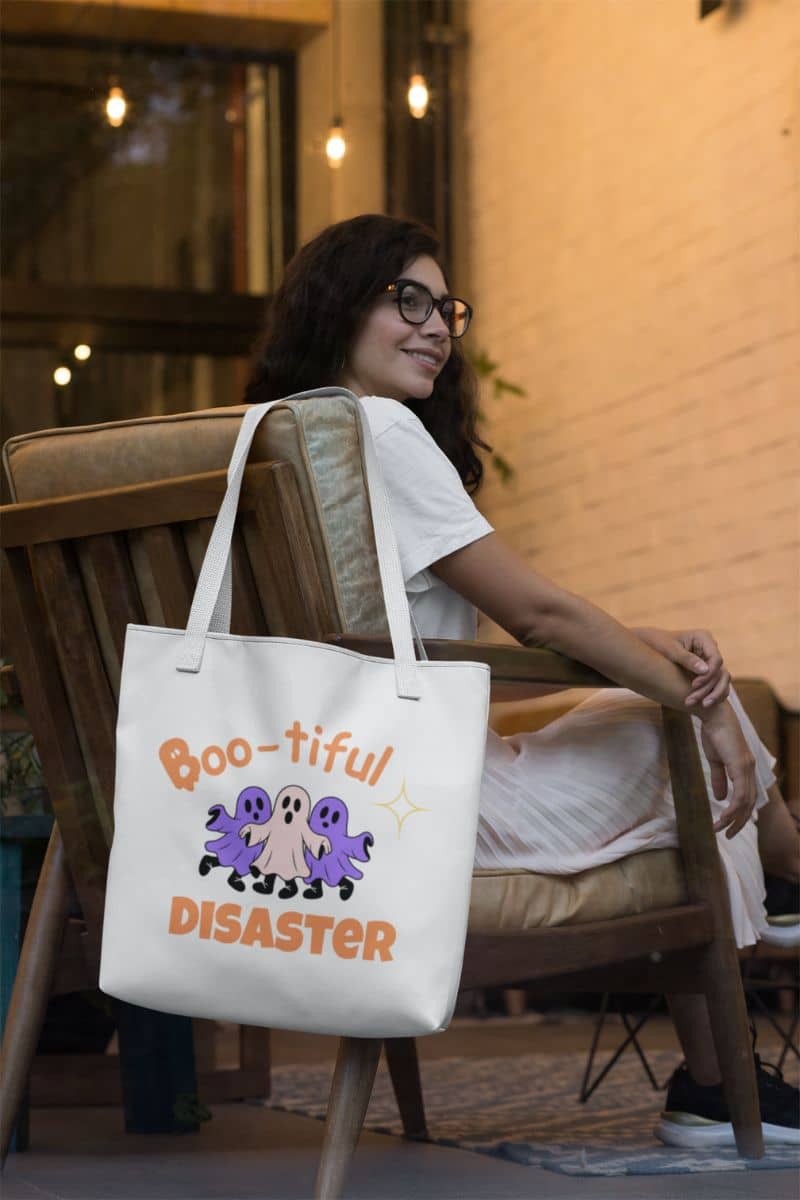 witchy tote bag with a woman sitting on a chair holding a tote bag with 'Boo-tiful Disaster' design.