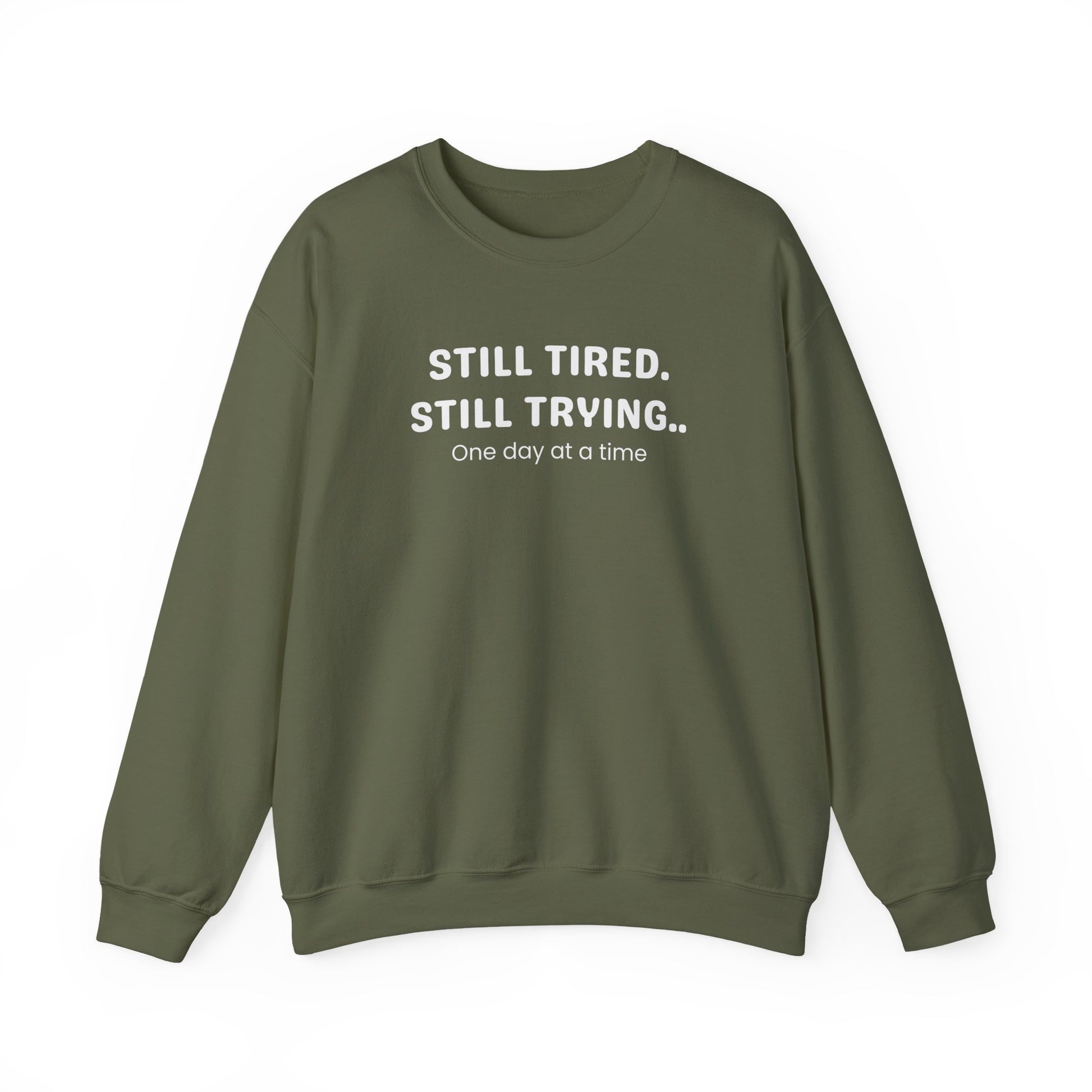 Green sweatshirt with text 'STILL TIRED. STILL TRYING.. One day at a time' on a white background