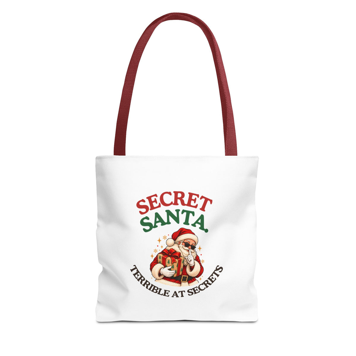 A white tote bag with red handles featuring the “Secret Santa. Terrible at Secrets.” design on a white background