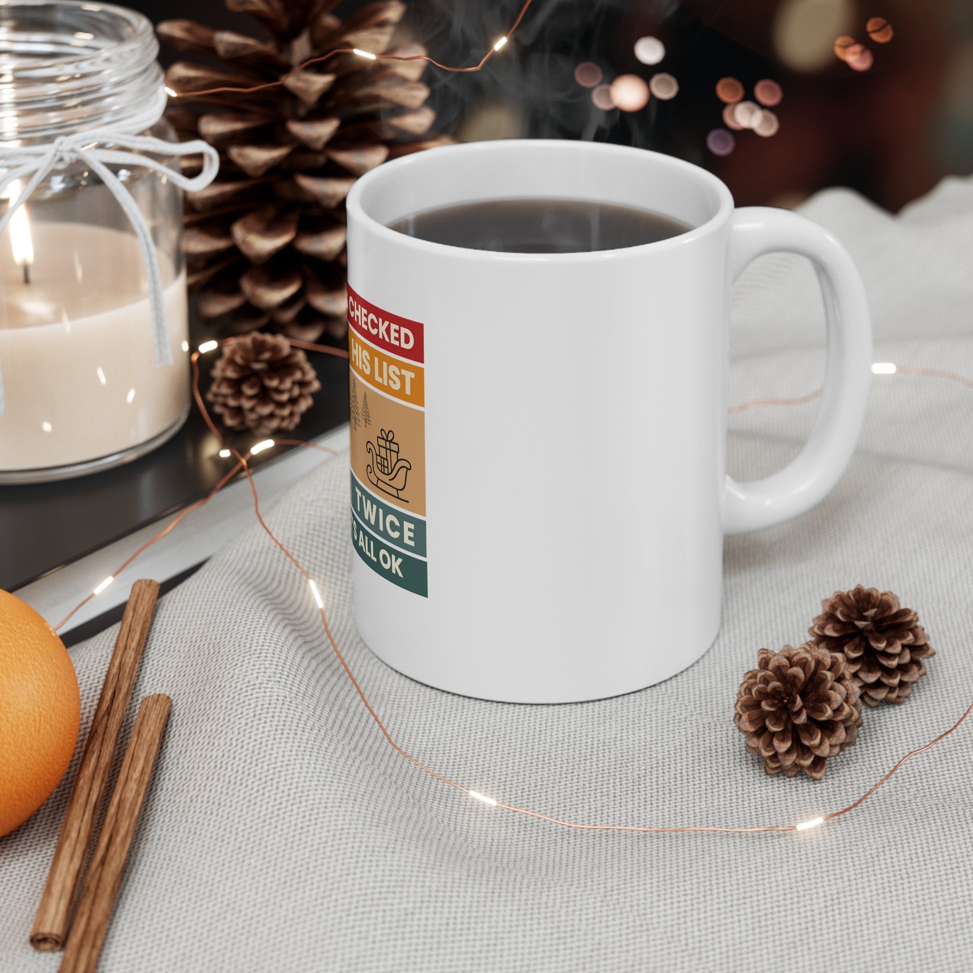 White mug with text 'Santa's Checked His List Twice And It's All Ok' on a table with decorative items