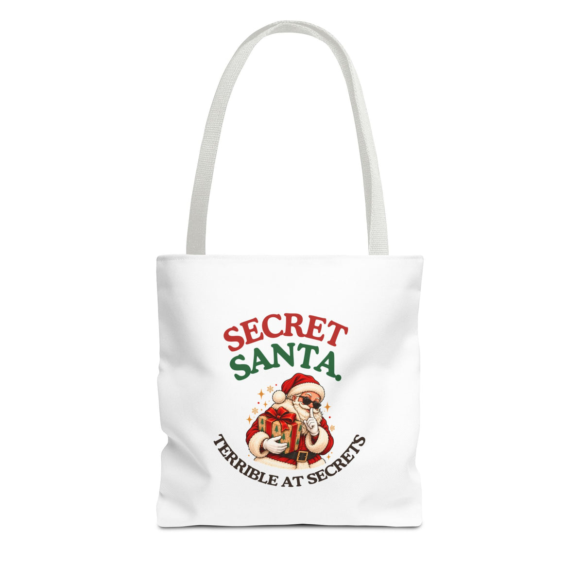 A white tote bag with white handles featuring the “Secret Santa. Terrible at Secrets.” design on a white background