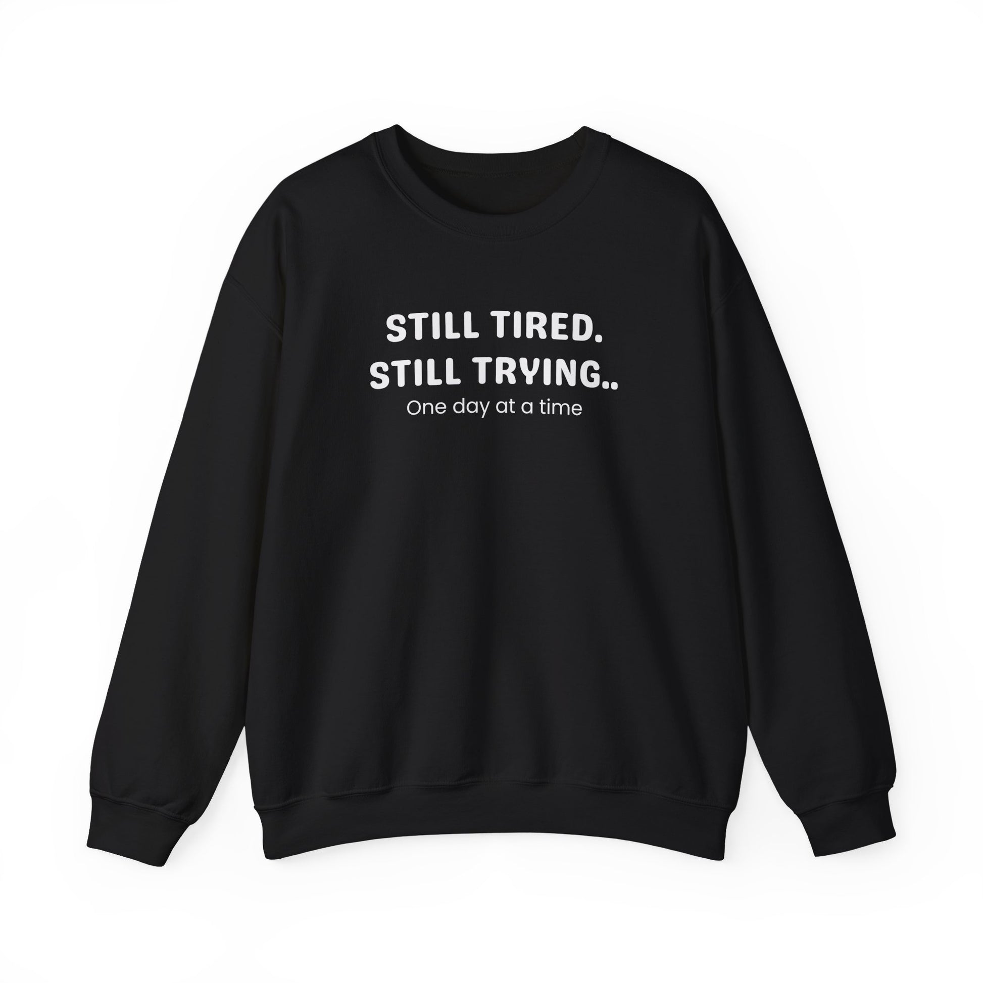 Black sweatshirt with text 'STILL TIRED. STILL TRYING.. One day at a time' on a white background