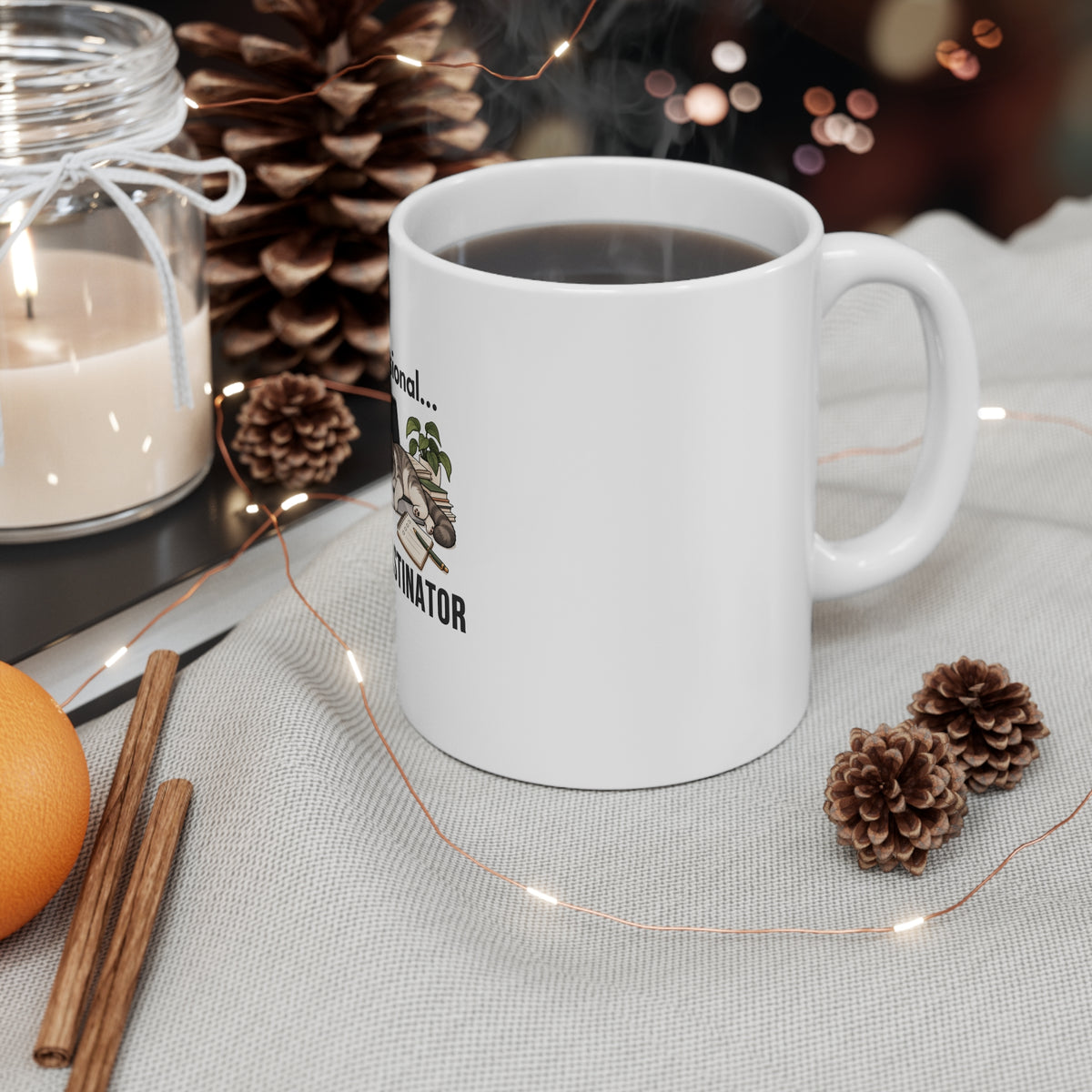 White mug with a Professional Procrastinator design on a table with a candle, orange, cinnamon stick, and pine cones.