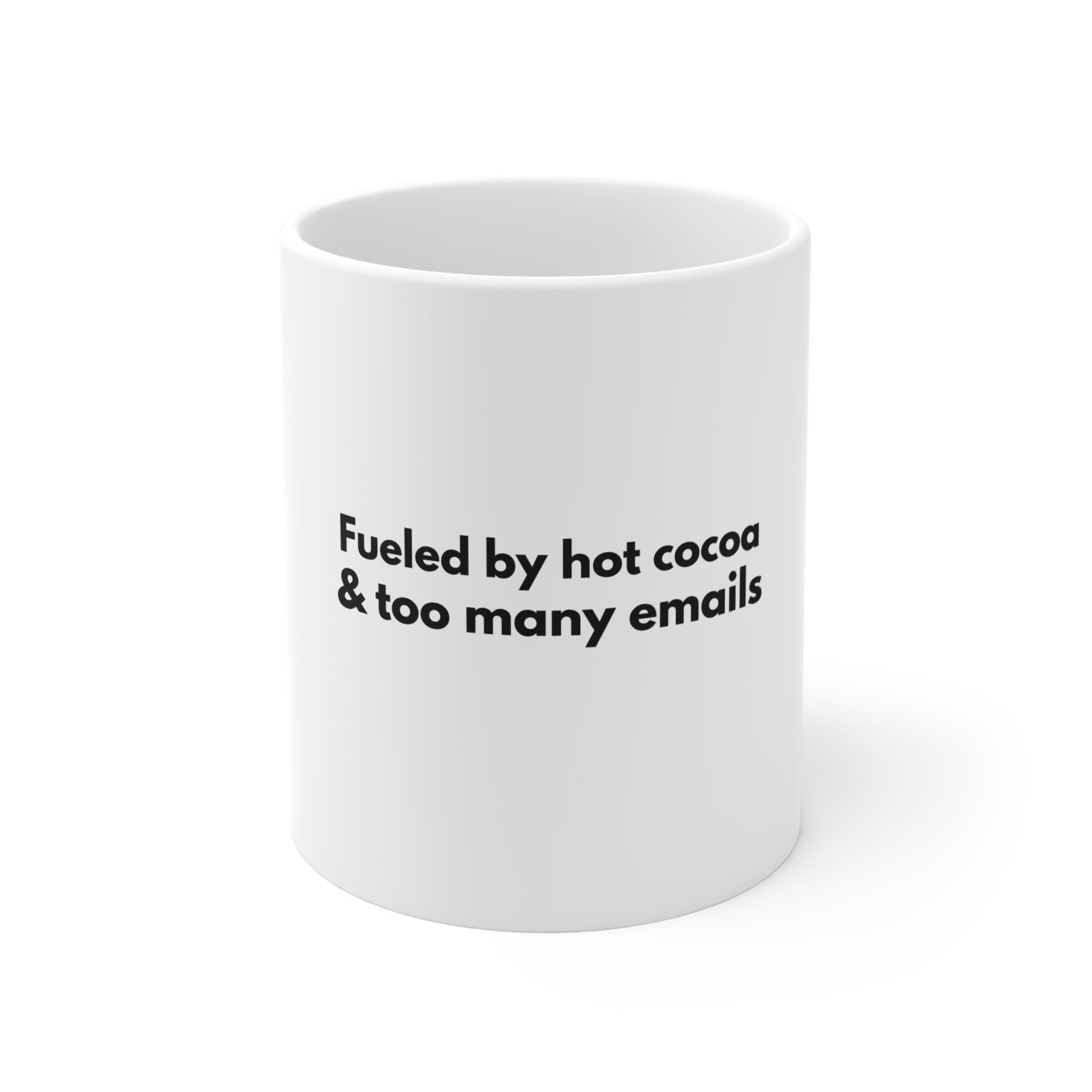 White mug with black text 'Fueled by hot cocoa & too many emails' on a white background