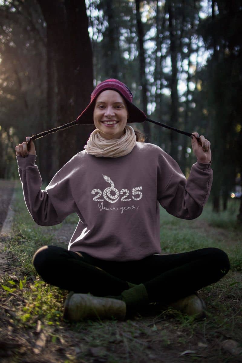 2025: Your Year Sweatshirt with a girl sitting in the woods posing with her wool hat