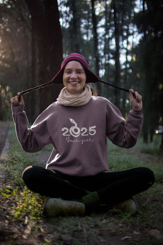 2025: Your Year Sweatshirt with a girl sitting in the woods posing with her wool hat
