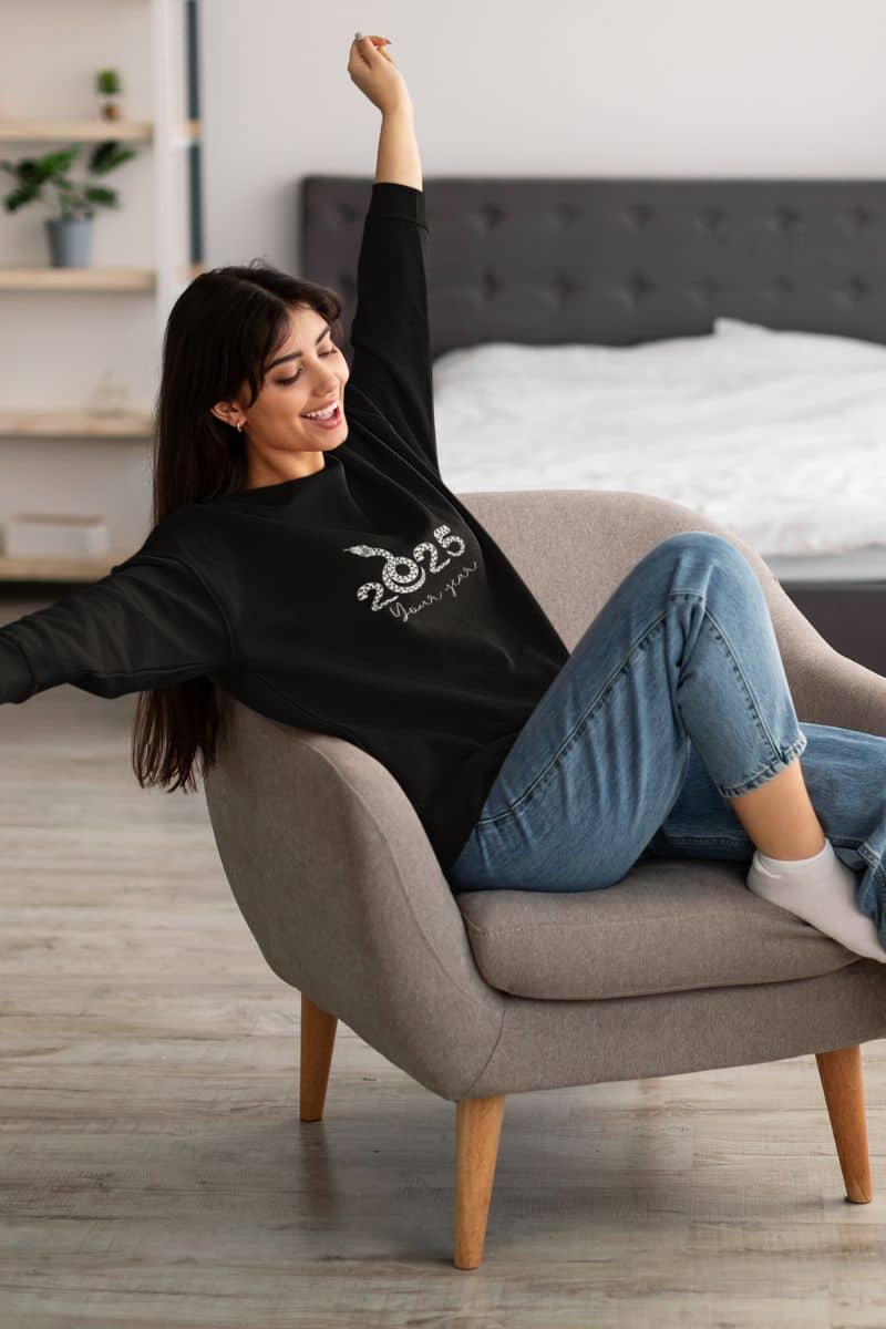 2025: Your Year Sweatshirt with a girl sitting and stretching her arms on the sofa