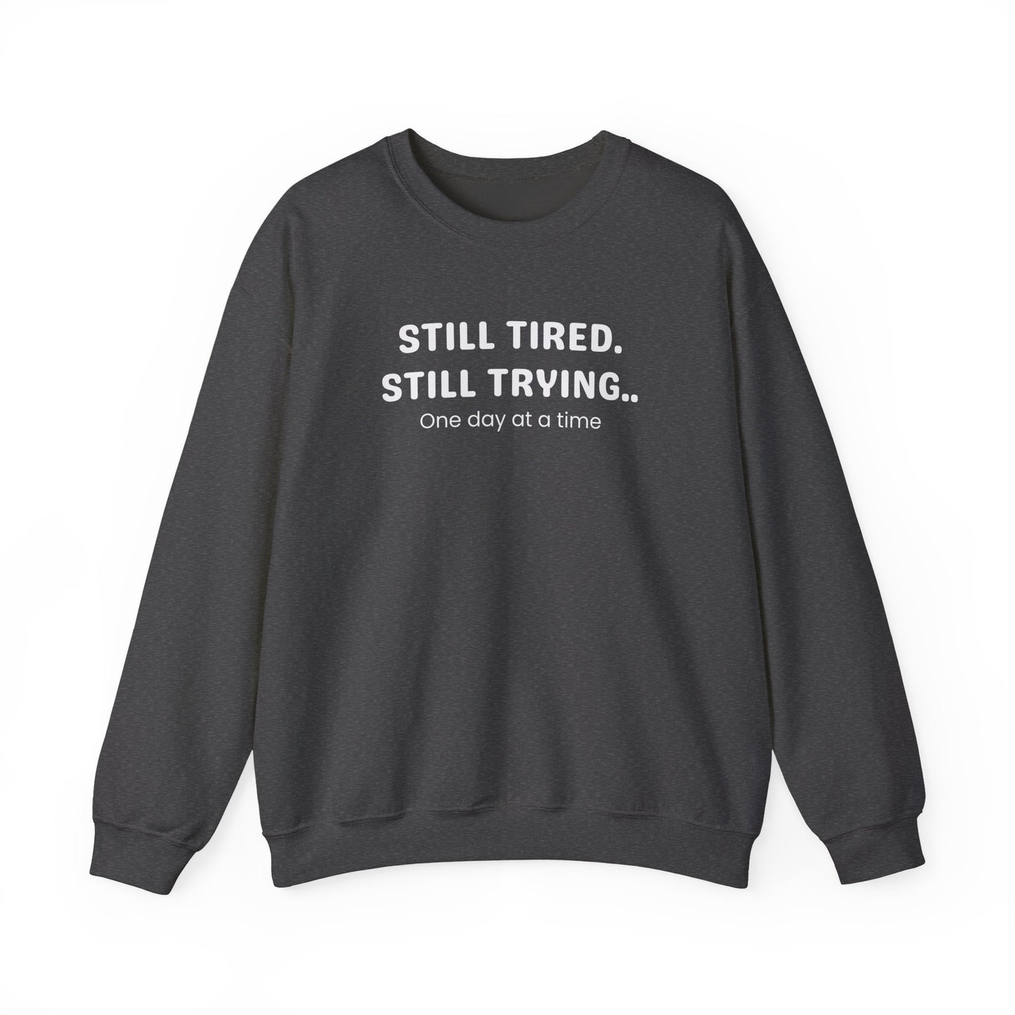 Dark gray sweatshirt with text 'STILL TIRED. STILL TRYING.. One day at a time' on a white background