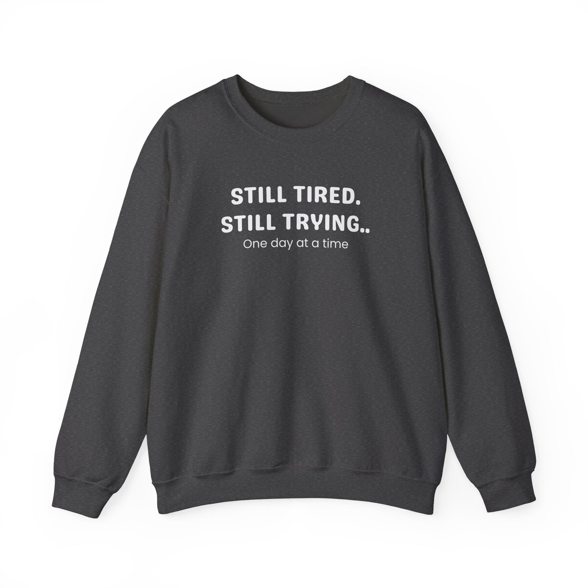 Dark gray sweatshirt with text 'STILL TIRED. STILL TRYING.. One day at a time' on a white background