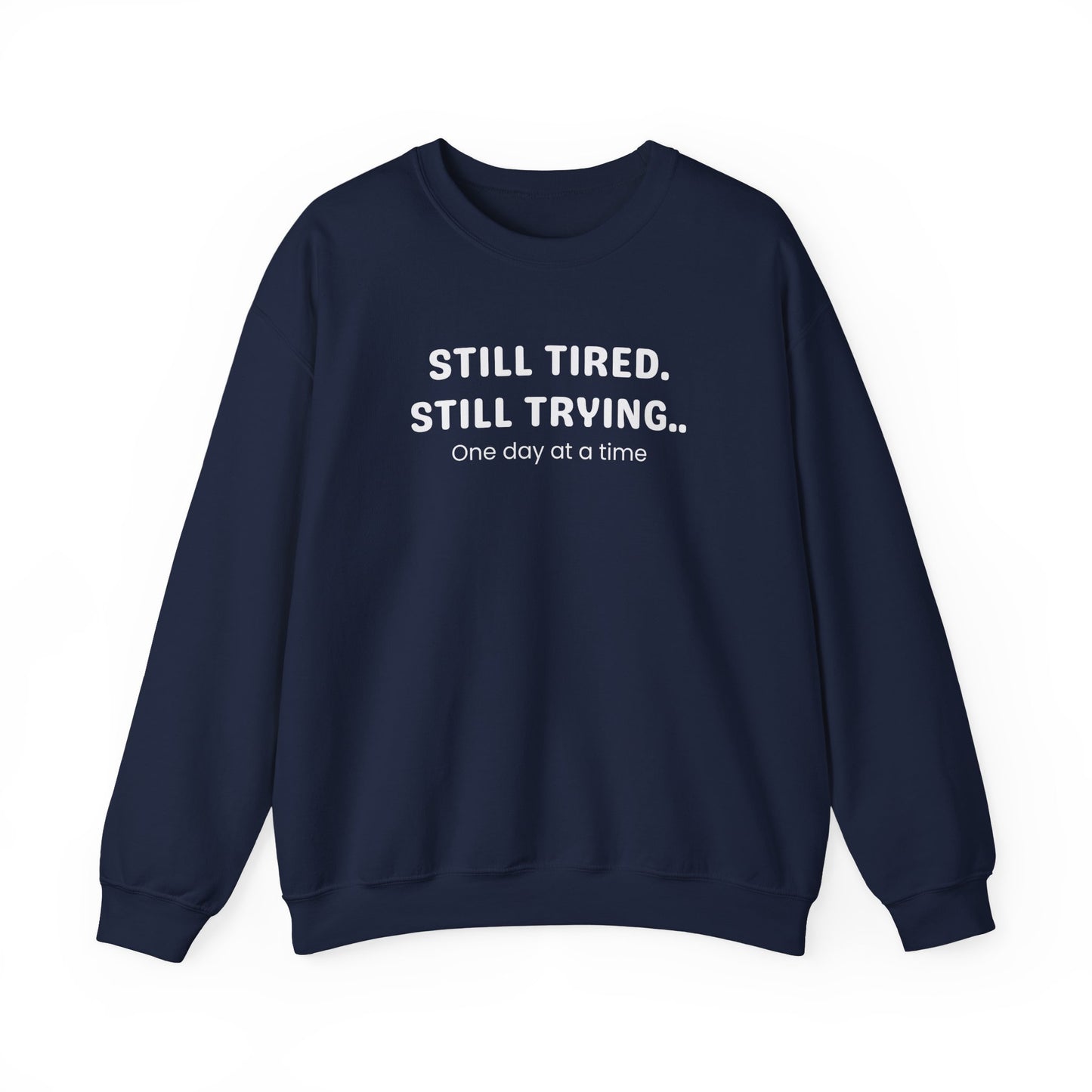 navy sweatshirt with text 'STILL TIRED. STILL TRYING.. One day at a time' on a white background