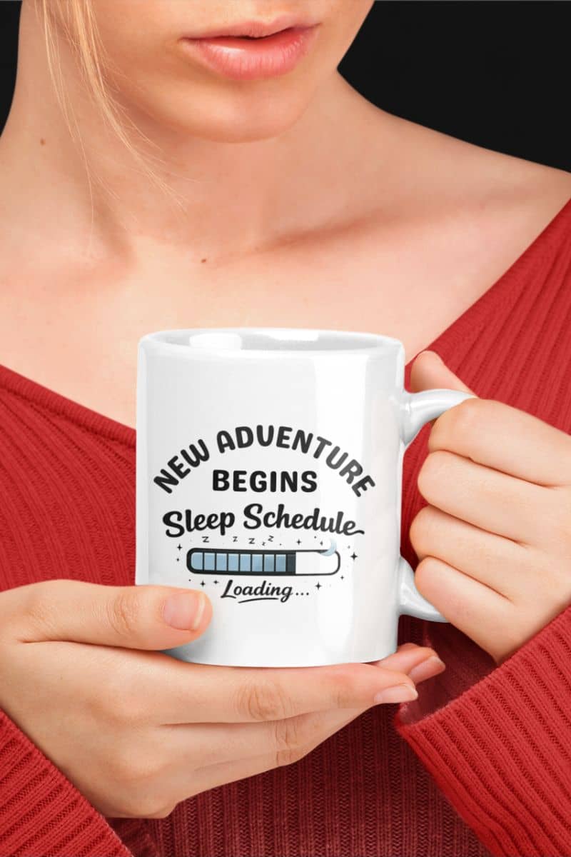 Always tired coffee mug with a person holding a white mug with text 'New Adventure Begins, Sleep Schedule Loading…', wearing a red sweater.