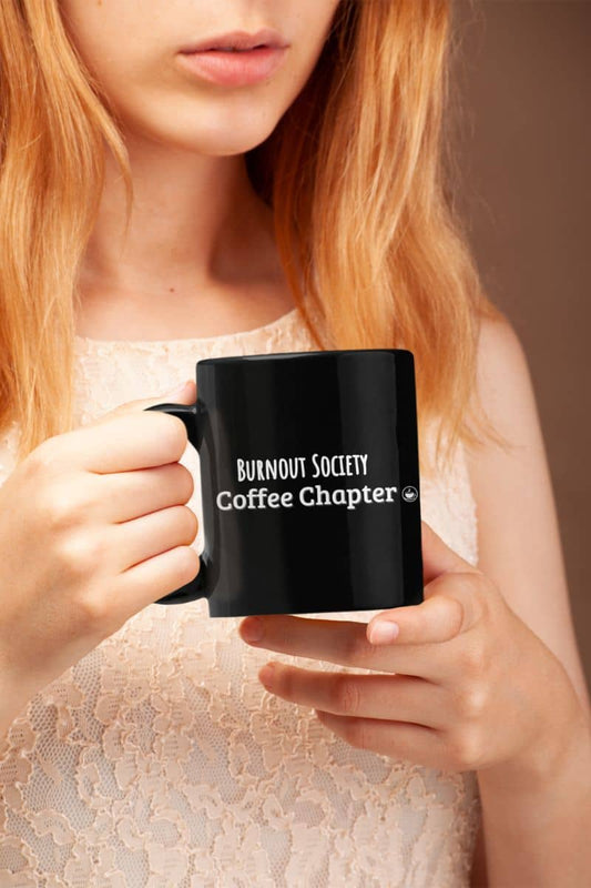 Burnout society coffee mug with a person holding a black mug with 'Burnout Society Coffee Chapter' text.