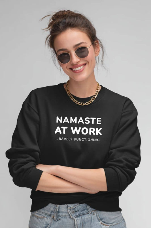 Burnout sweatshirt with a woman wearing a black sweatshirt with 'Namaste at Work...Barely Functioning' text on a plain background