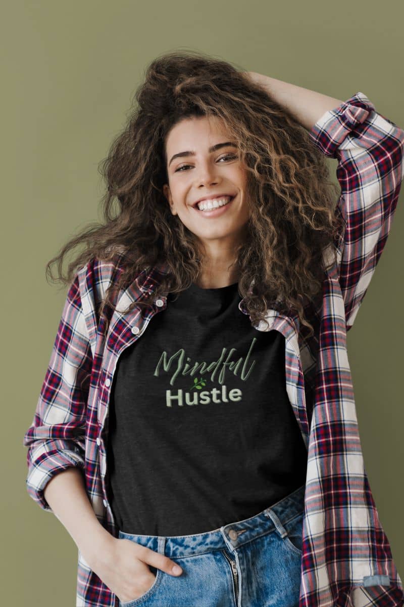 Business motivation shirt with a woman wearing a black t-shirt with 'Mindful & Hustle' text, plaid shirt, and jeans on a green background
