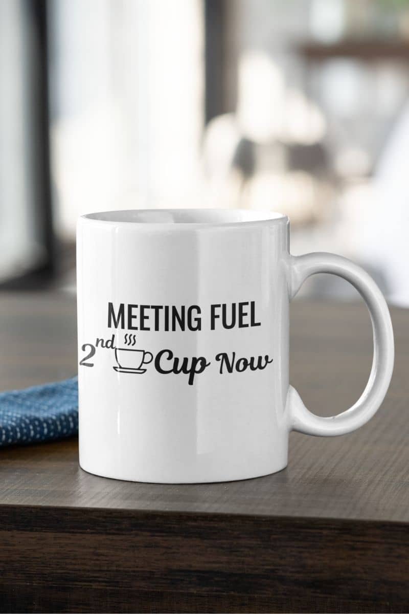 Caffeine mug with a white mug with text 'Meeting Fuel: 2nd Cup Now' on a wooden surface.