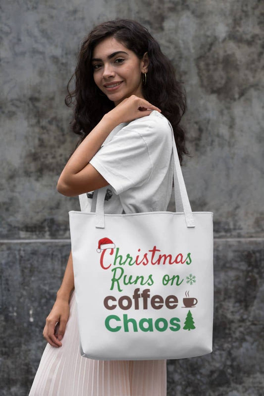 Christmas coffee lover tote with a woman holding a tote bag with text 'Christmas Runs on Coffee Chaos' text against a gray wall.