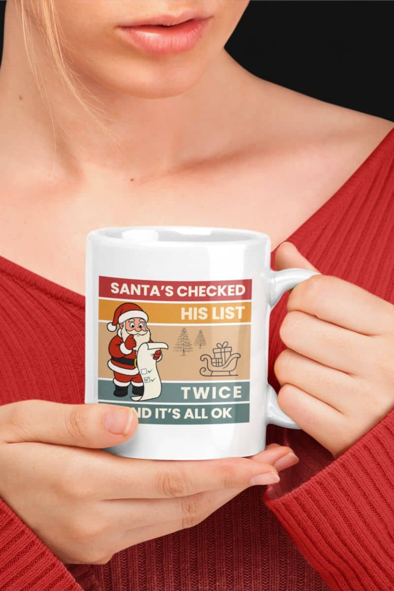 Christmas mug with a person holding a mug with a Christmas-themed design featuring the text 'Santa's Checked His List Twice And It's All Ok'