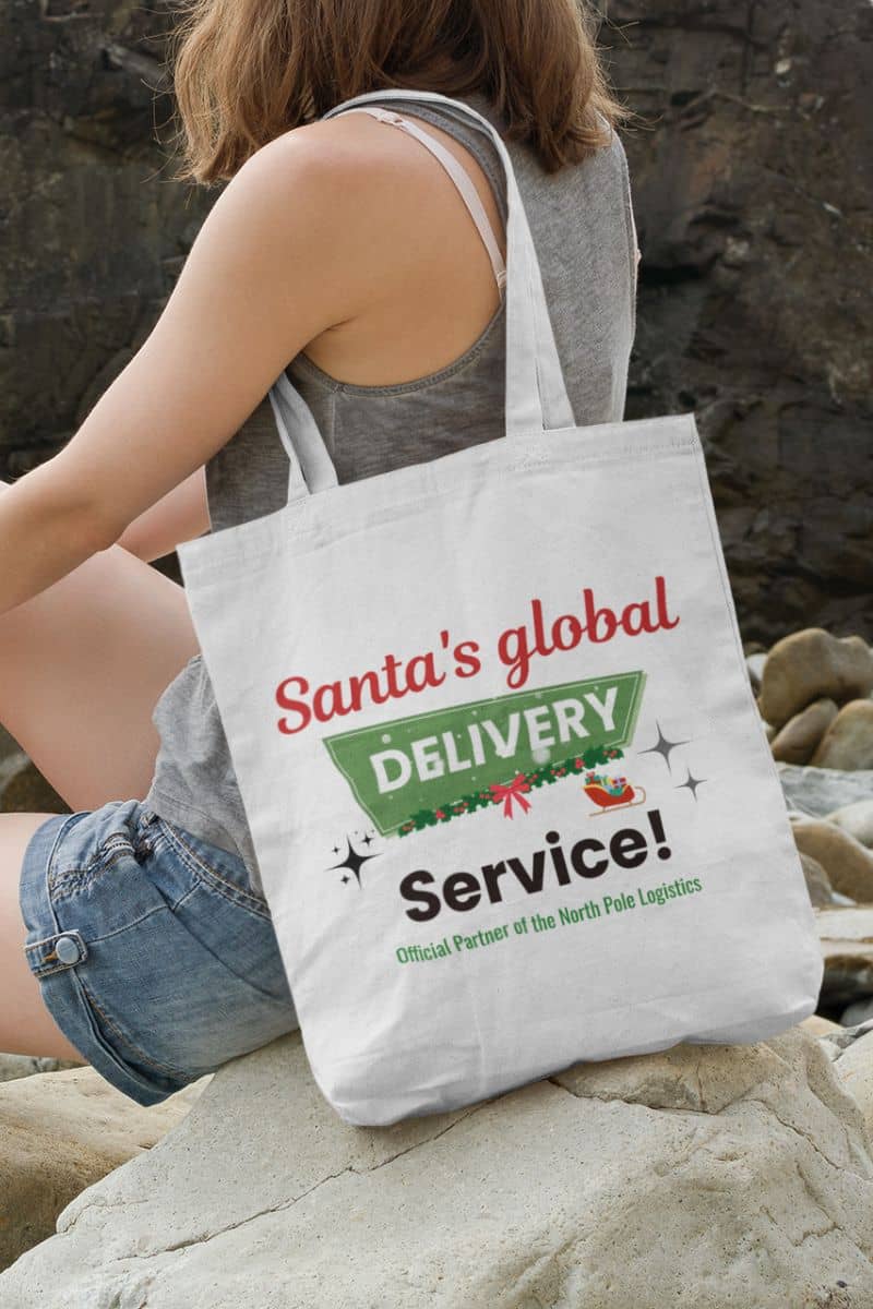 Christmas tote bag gift with a girl wearing a tote bag with text 'Santa's Global Delivery Service.', sitting on the rock