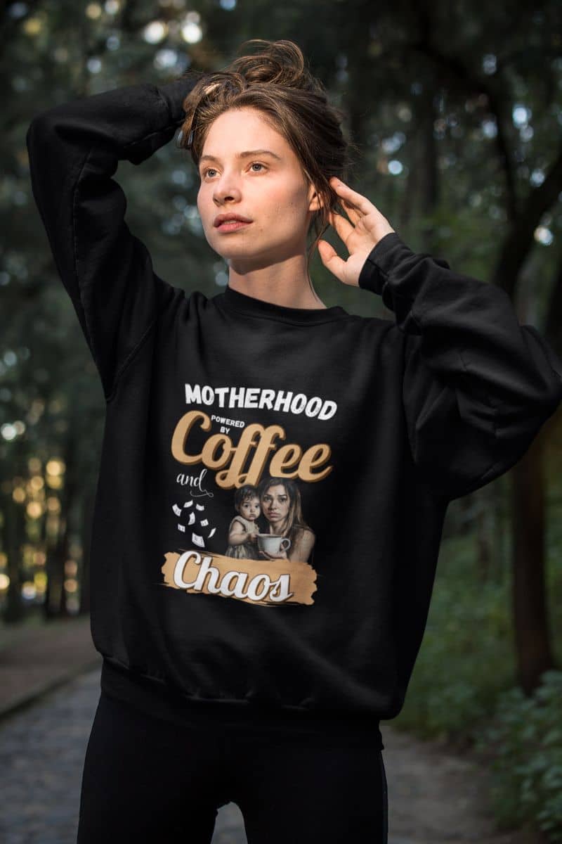 Coffee and chaos sweatshirt with a person wearing a black sweatshirt with text 'Motherhood powered by Coffee and Chaos' and a graphic in a forest setting