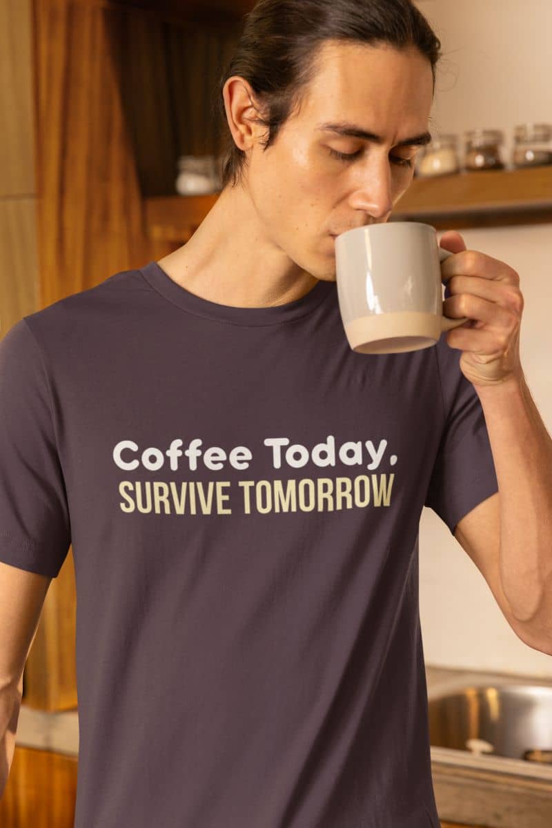 Coffee humor t-shirt with a man in a t-shirt with 'Coffee Today, Survive Tomorrow' text, drinking from a mug in a kitchen.