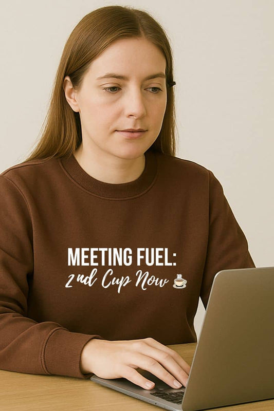 Coffee lover sweatshirt with a person wearing a brown sweatshirt with text 'Meeting Fuel: 2nd Cup Now' sitting at a laptop.