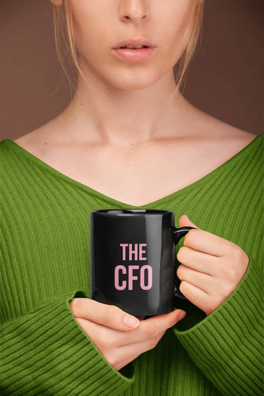 Coffee mug for women with a person holding a black mug with 'THE CFO' in pink text against a brown background