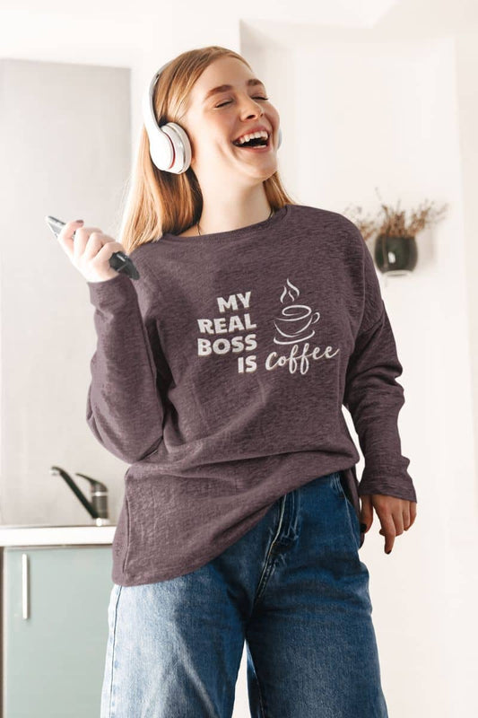 Coffee sweatshirt with a girl wearing a sweatshirt with 'My real boss is coffee' text in a kitchen.
