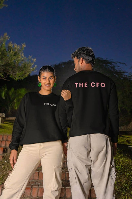 Couple sweatshirt with two people wearing black sweatshirts with 'THE CEO' and 'THE CFO' text, standing outdoors at night.