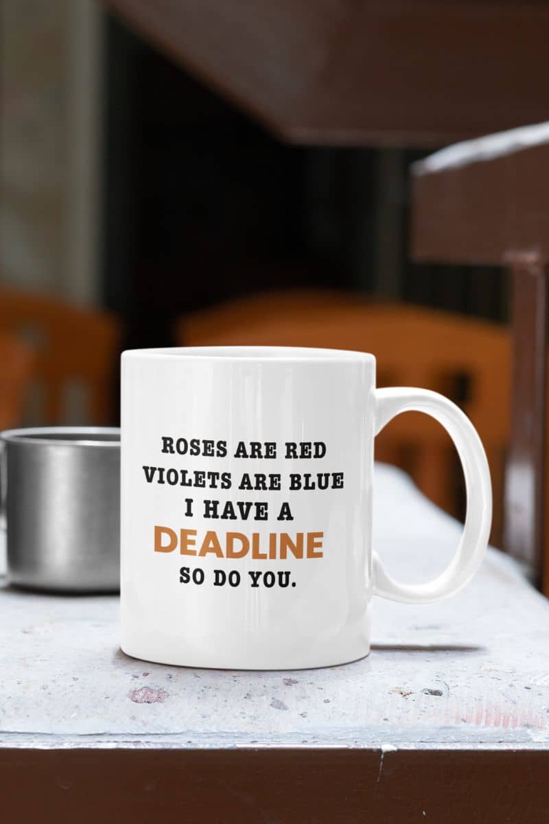Coworker coffee mug with a white mug with text 'Roes are red, violets are blue. I have a deadline so you do' on a table in a casual setting