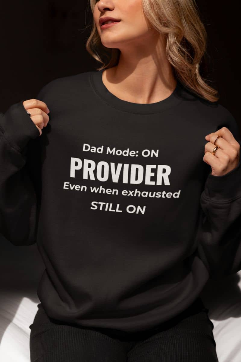 Dad crewneck sweatshirt with a woman wearing a sweatshirt featuring the text 'Dad Mode: On. Provider. Even when exhausted. Still on'