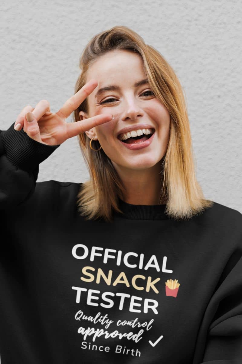 Food sweatshirt with a person wearing a black sweatshirt featuring the text 'Official Snack Tester – Quality Control Approved – Since Birth', making a peace sign.
