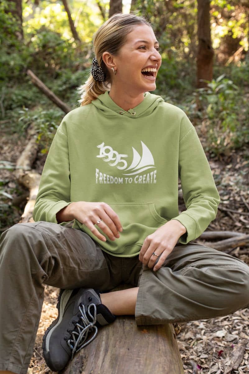 Freedom to Create Unisex Hooded Sweatshirt with a girl sitting on a dry tree stump with a bright smile