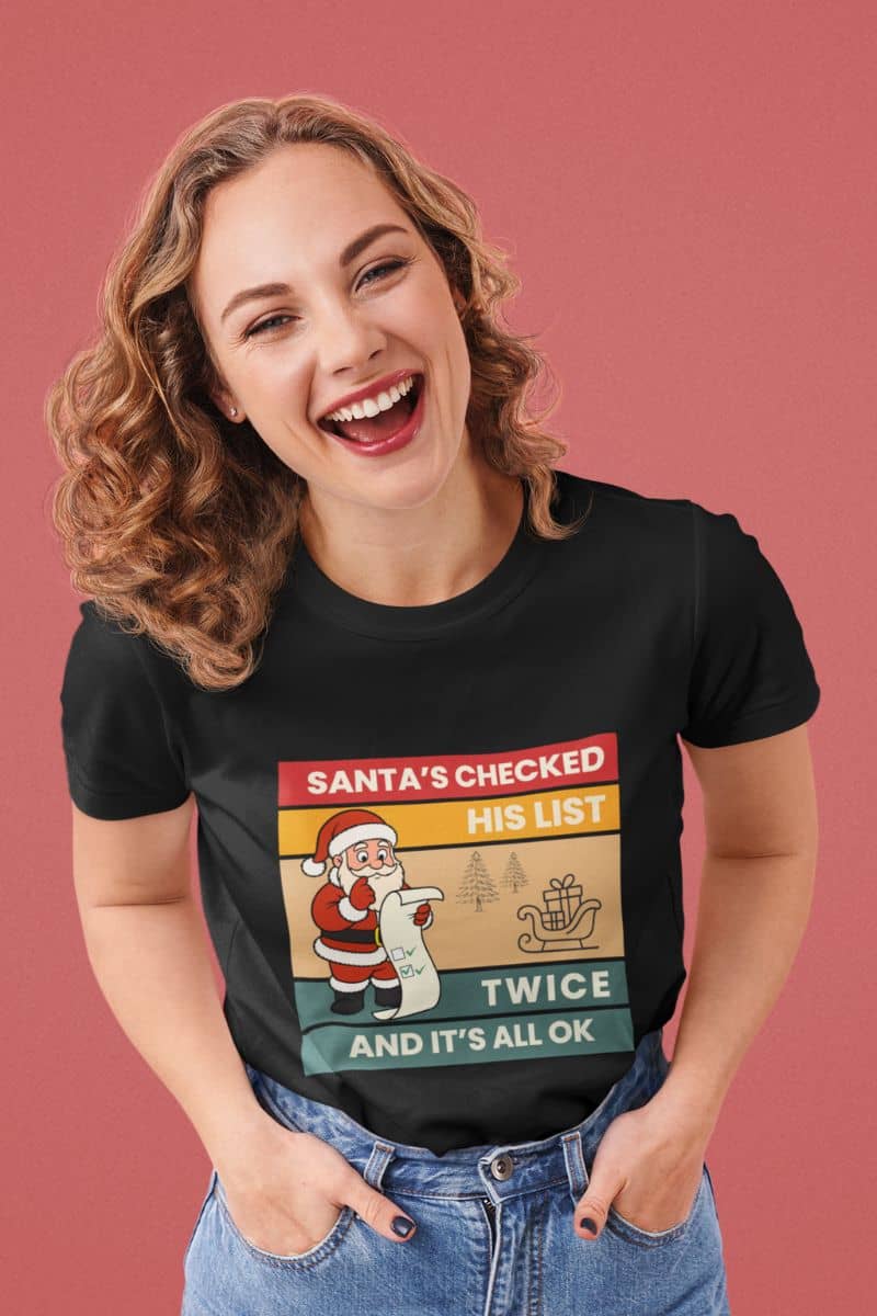 Funny Christmas T-Shirt for adults with a woman in a black t-shirt text 'Santa's Checked His List Twice And It's All Ok'.