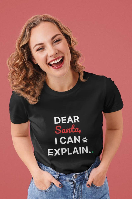 Funny Christmas t-shirt with a woman wearing a black t-shirt with text 'Dear Santa, I can explain.' on a pink background