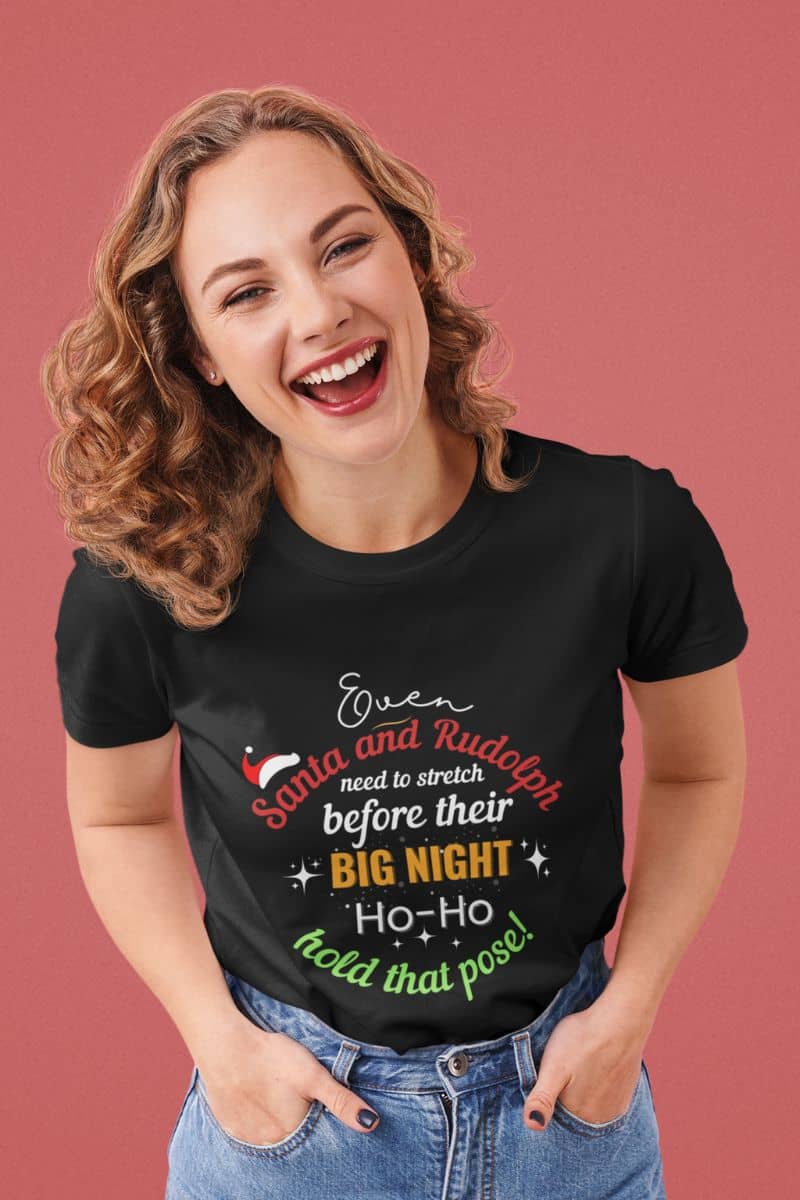 Funny Christmas yoga shirt with a woman wearing a black t-shirt with text 'Event Santa & Rudolph Need to Stretch Before their Big Night. Ho-Ho-Hold That Pose!' on a red background