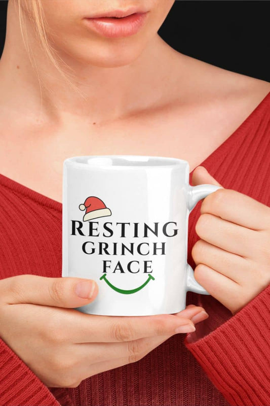 Funny Grinch Christmas mug with a person holding a white mug with 'Resting Grinch Face' text and Santa hat design.