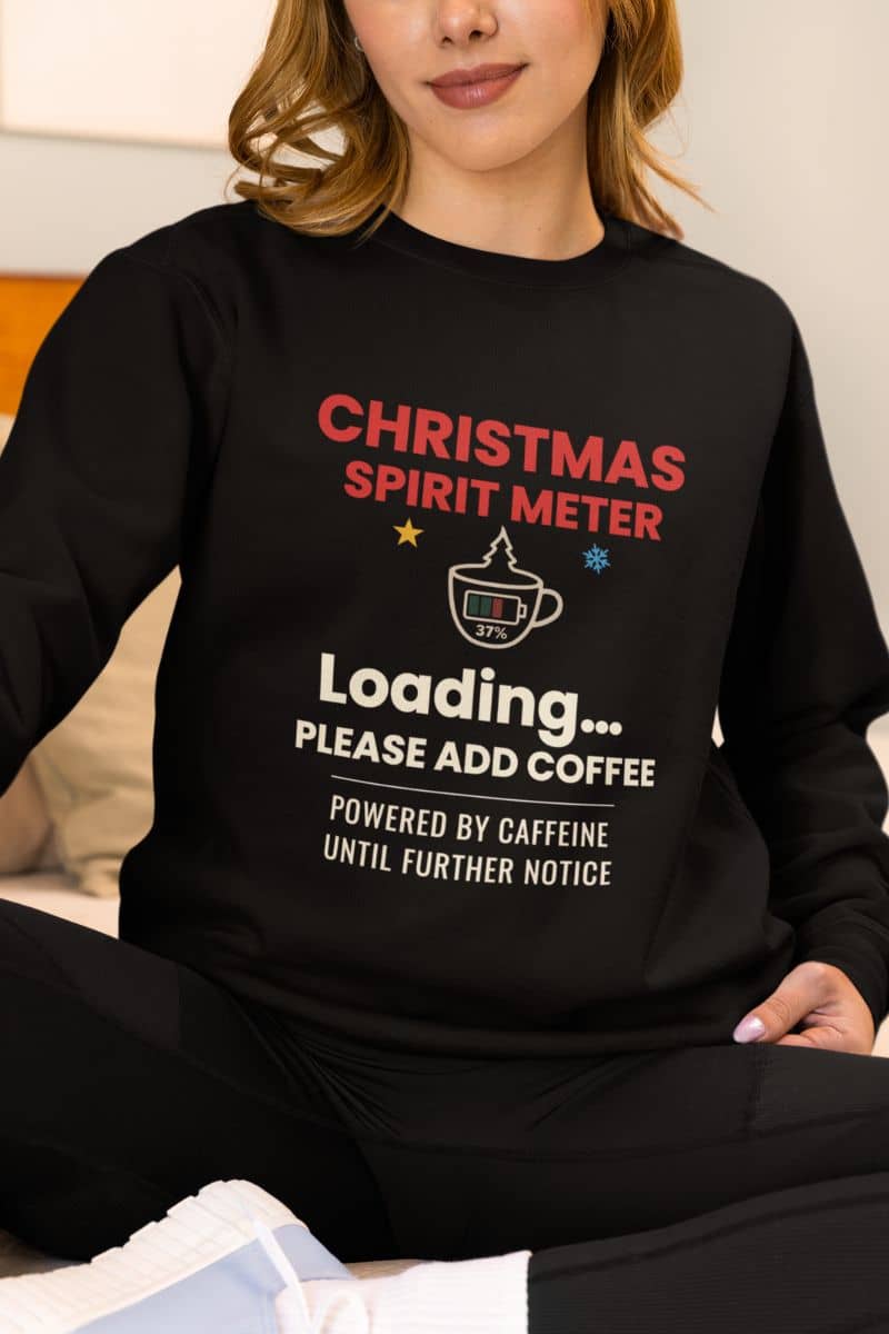 Funny holiday caffeine sweatshirt with a person wearing a black sweatshirt with text 'Christmas Spirit Meter, Loading…37%. Please add coffee. Powered by caffeine until further notice'