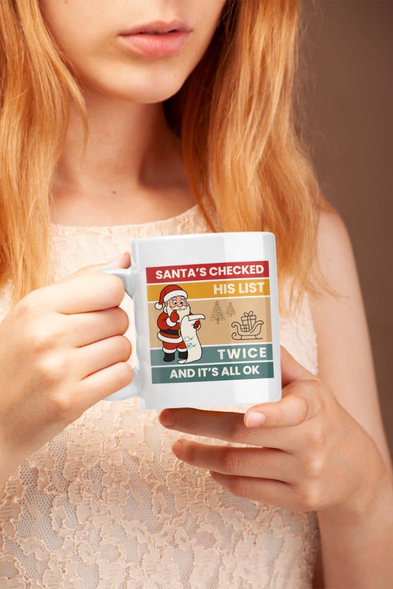 Funny Santa mug with a person holding a mug with a Santa Claus design and text 'Santa's Checked His List Twice And It's All Ok'.