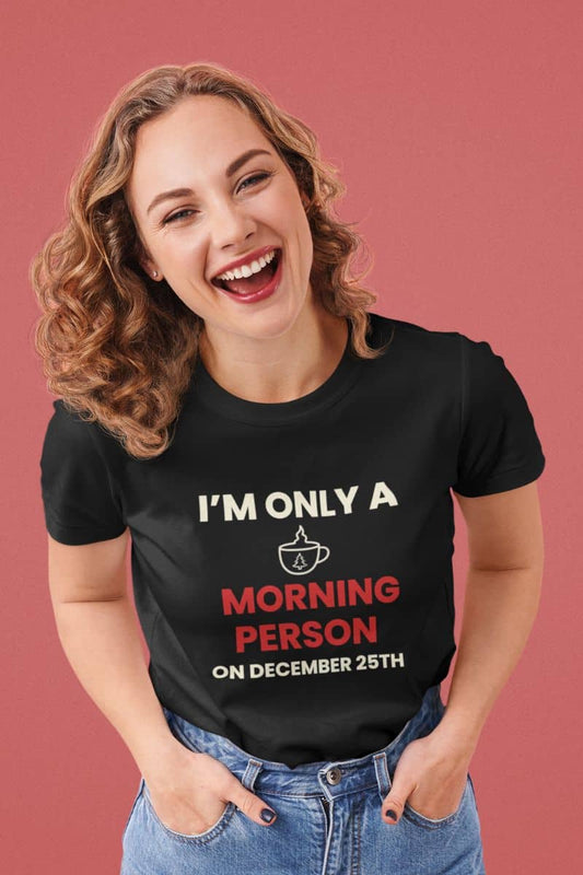 Funny christmas morning shirt with a woman wearing a black t-shirt with text 'I’m Only a Morning Person on December 25th' on a pink background