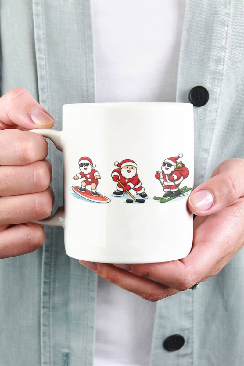 Funny christmas sports mug with a person holding a mug with three cartoon Santas on it, wearing different sports outfits.