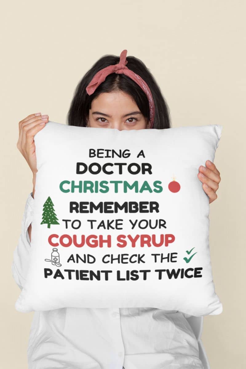 Funny doctor christmas pillow with a person holding a pillow with text 'Being a doctor during Christmas, remember to take your cough syrup and check the patient list twice'.