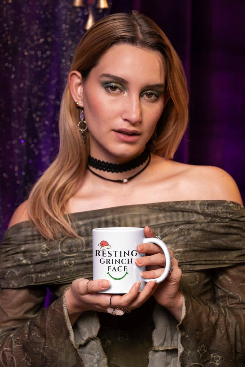 Funny gift for coworkers with a woman holding a mug with 'Resting Grinch Face' text against a purple curtain background