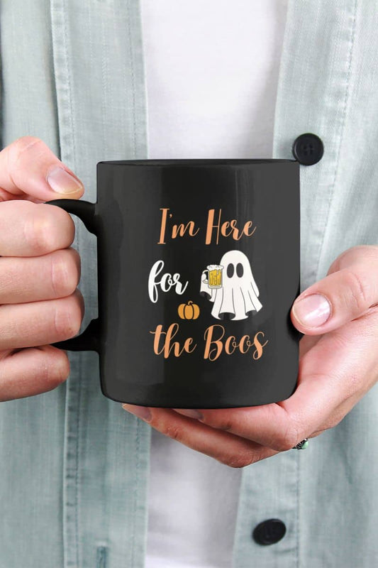 Funny halloween mug with black mug with Halloween design held by a person, featuring text 'I’m Here for the Boos'