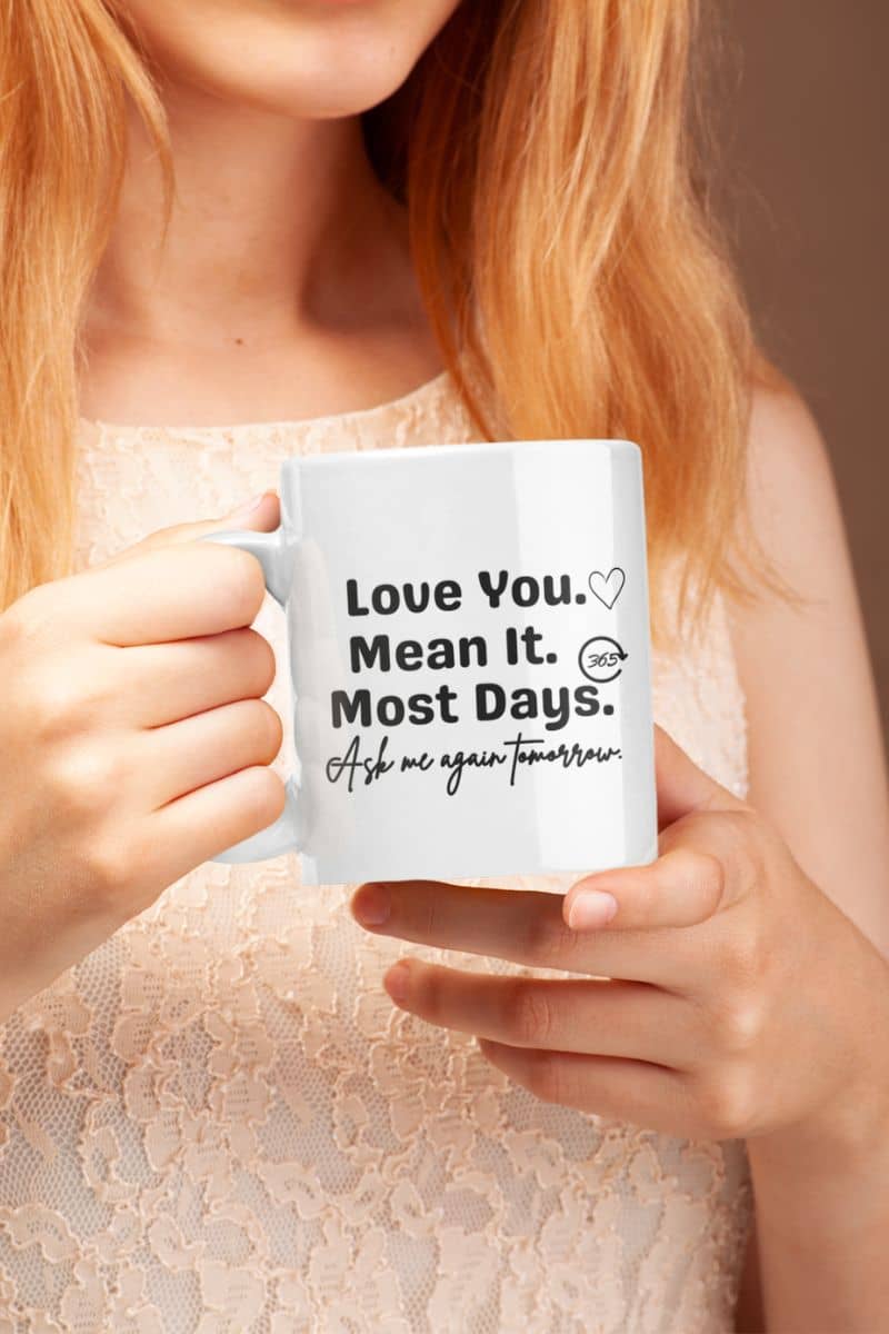 Funny love coffee mug with a person holding a mug with text 'Love You. Mean It. Most Days. Ask me again tomorrow.'