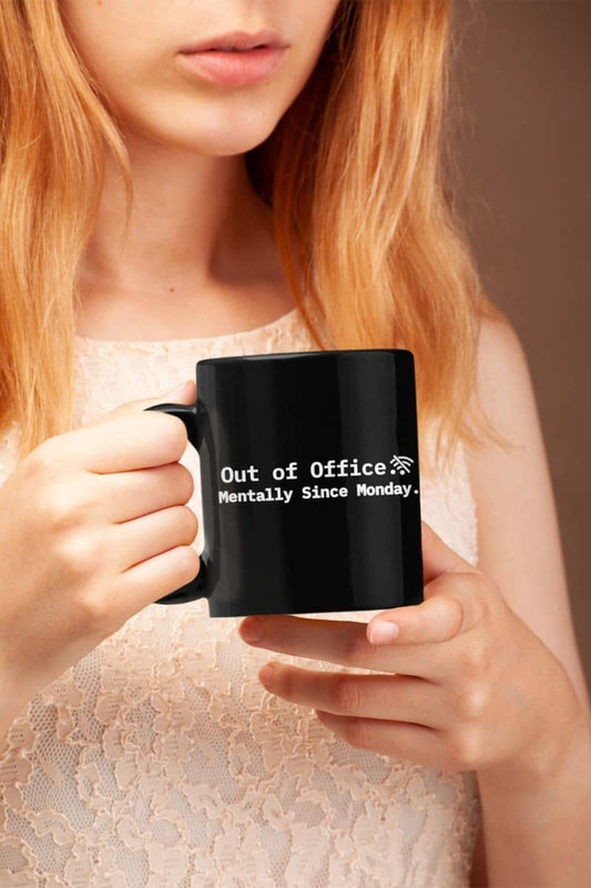 Funny mental health mug with a person holding a black mug with humorous text 'Out of Office. Mentally Since Monday'